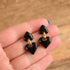 Black heart-shaped earrings held in a hand against a wooden background